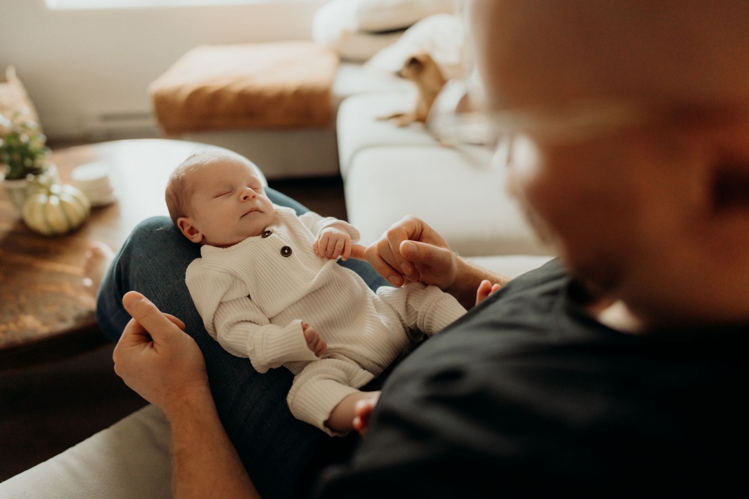A sleeping newborn dressed in a white ribbed onesie with buttons in a cozy indoor setting.