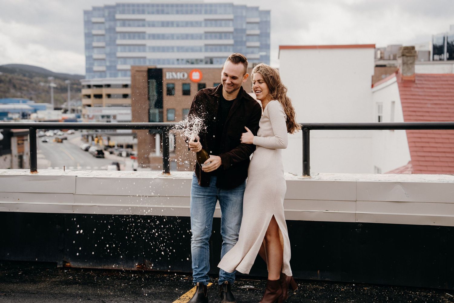 A couple shares a romantic moment on an urban rooftop with city buildings in the background.