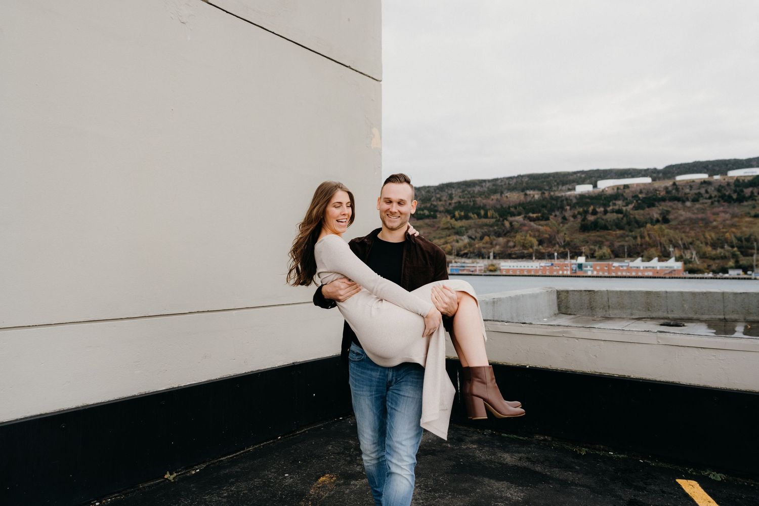A couple poses playfully on a rooftop parking structure with mountain views.