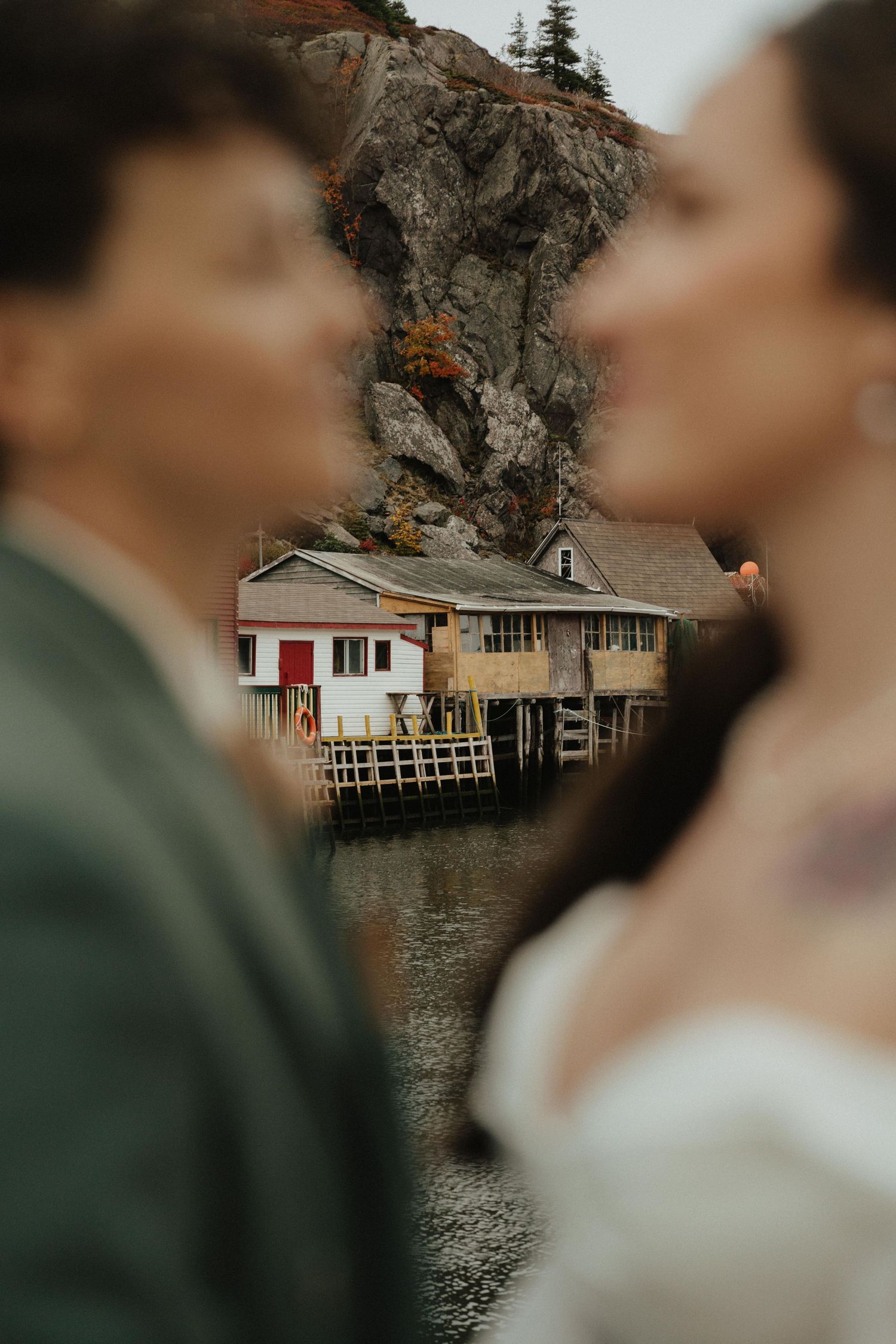 A romantic lakeside scene with a rustic boathouse on stilts over calm waters at sunset.