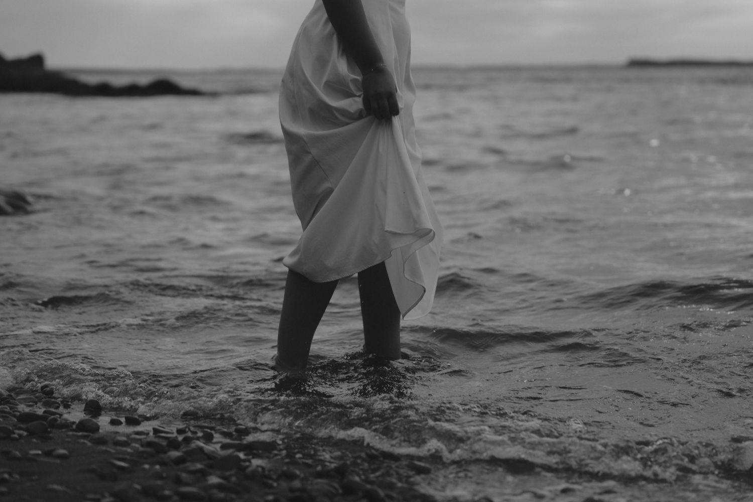 Couple walking hand in hand along a misty beach shoreline at sunset with waves lapping at their feet.