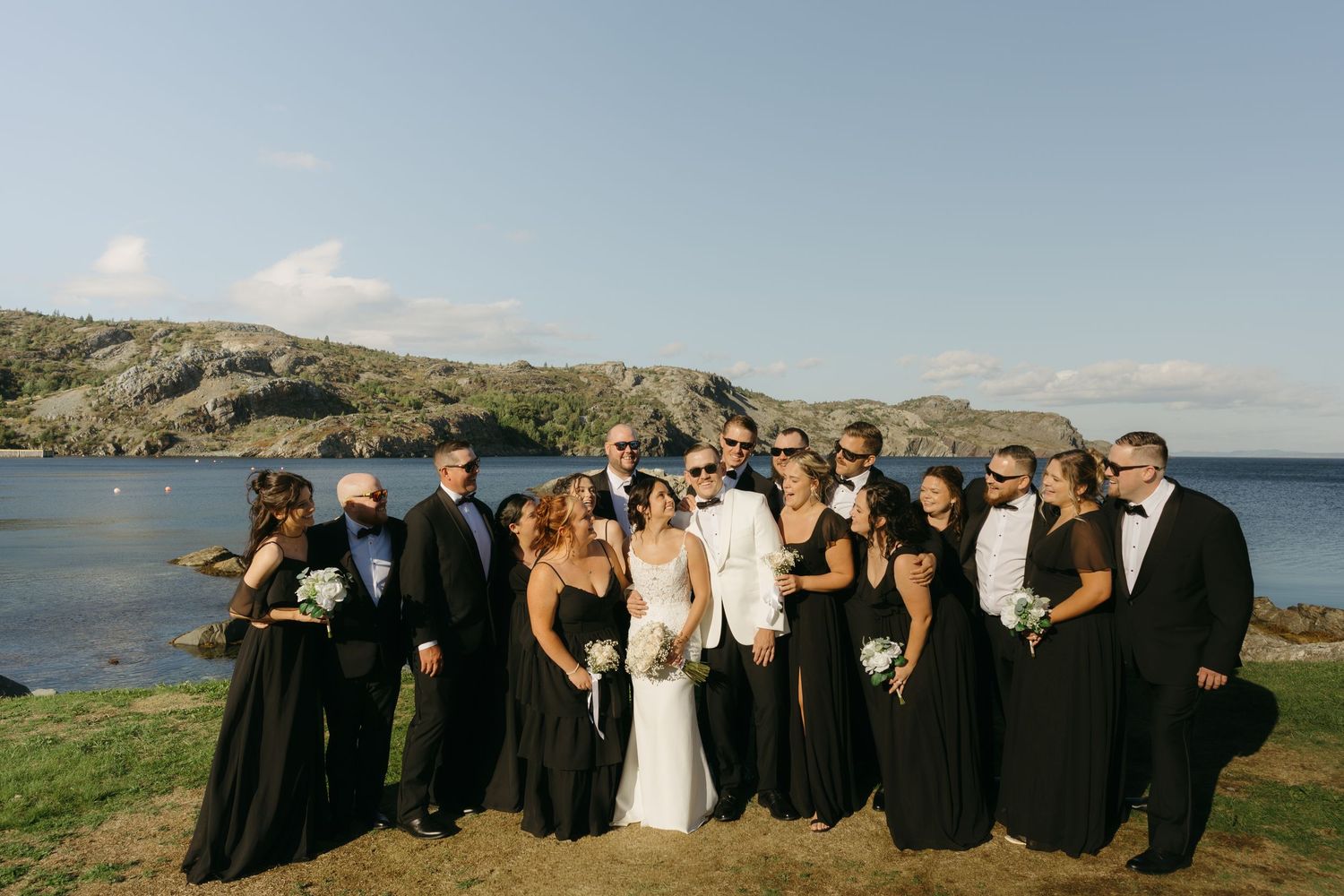 Wedding party poses together against scenic coastal landscape during sunset celebration.