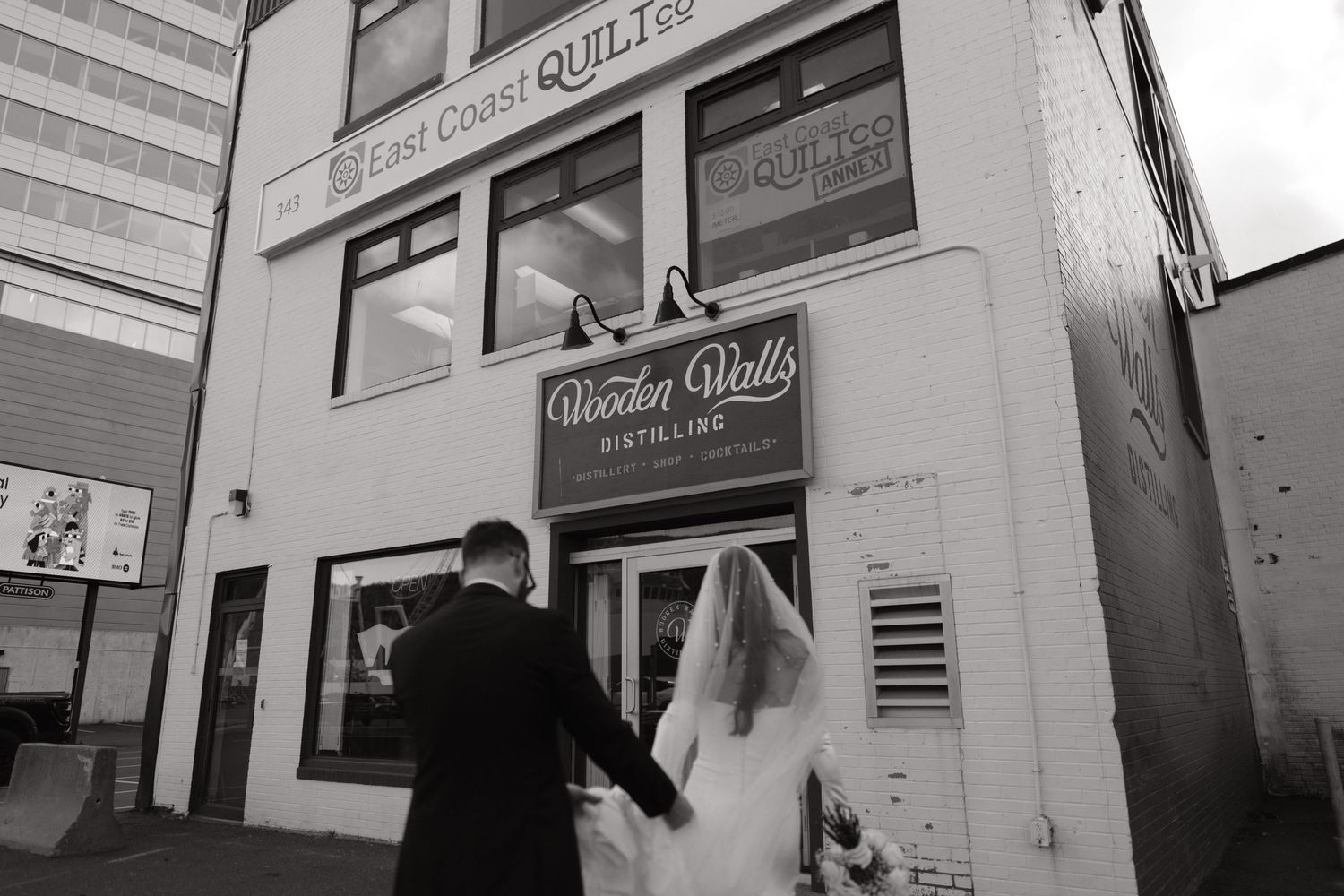 Bride and groom holding hands outside Wooden Walls Distilling in black and white wedding photo.