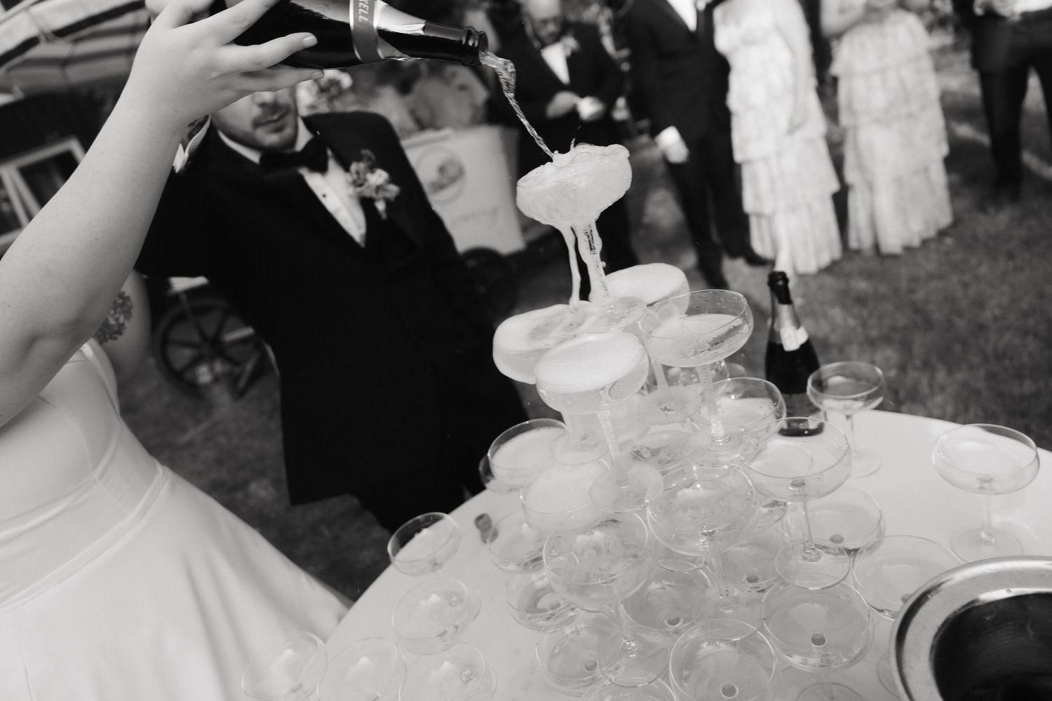 Crystal champagne glasses stacked in a pyramid formation at an outdoor event.