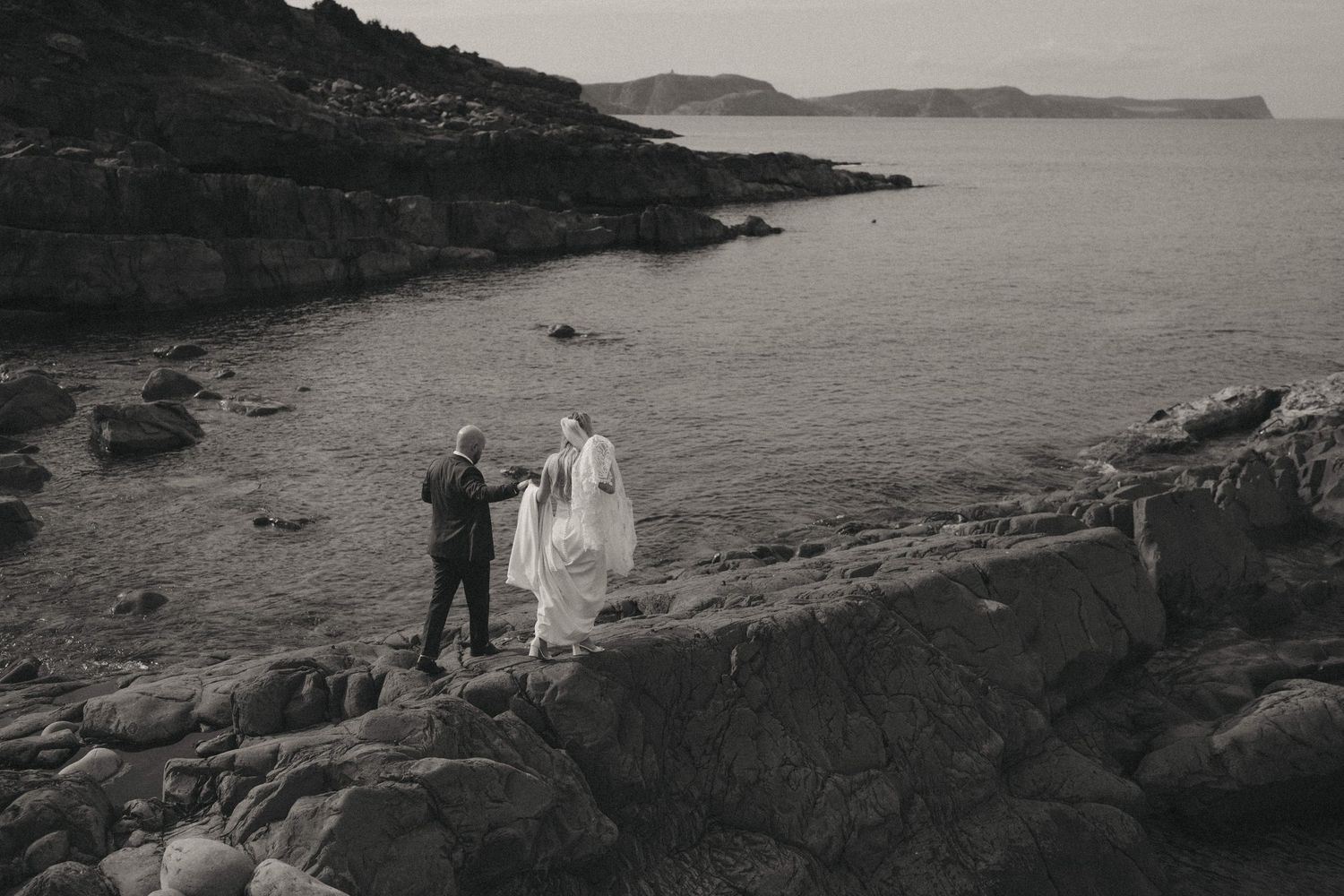 Wedding couple photographed on rugged coastal rocks with sweeping ocean views.