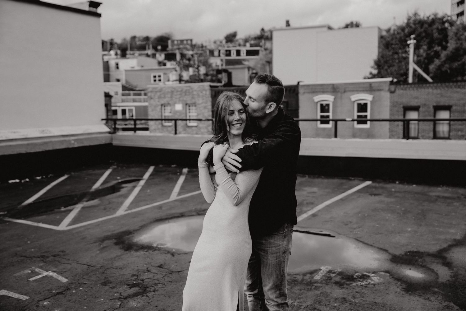 Black and white photo of couple sharing tender moment against urban skyline backdrop.