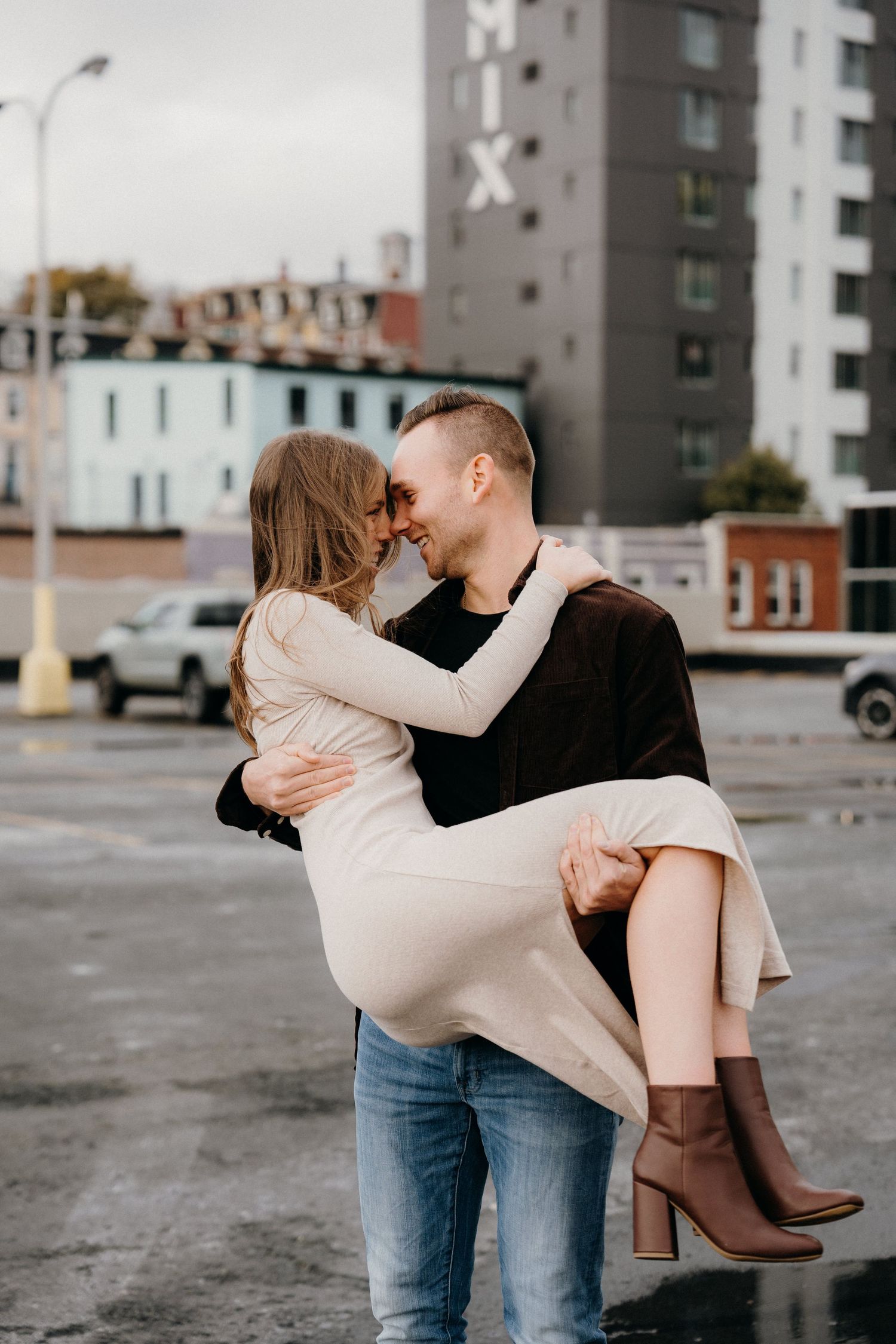 Intimate dance pose captured in an industrial urban setting with gray buildings and cloudy sky.