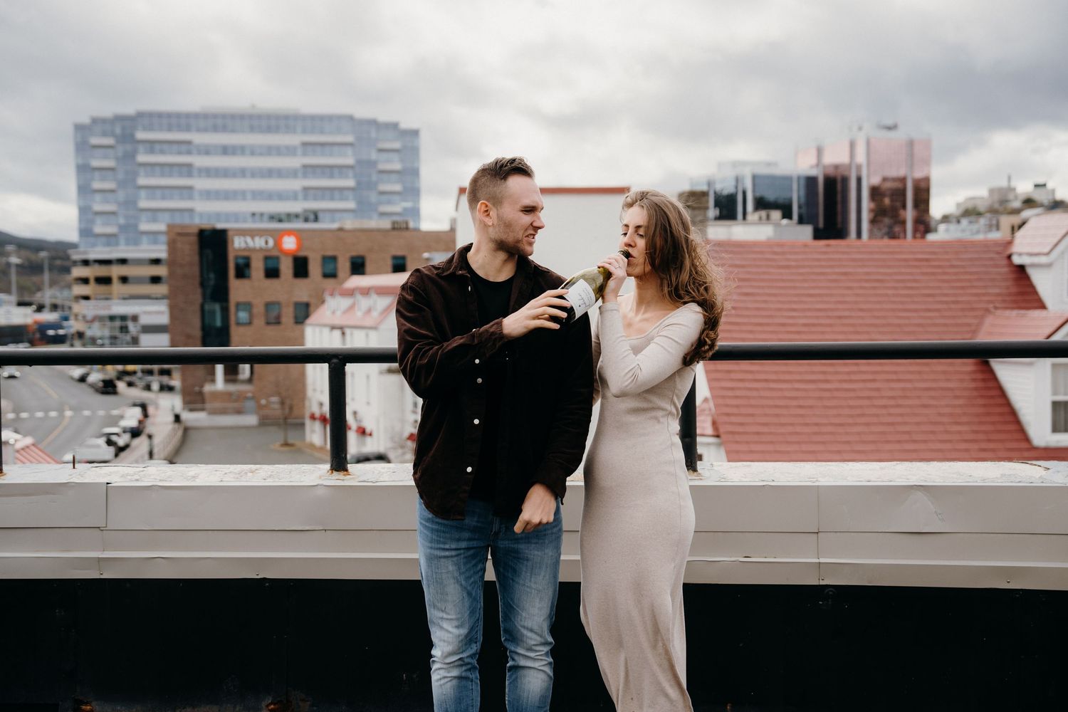Two people share a playful moment on a rooftop with city skyline visible in the distance.