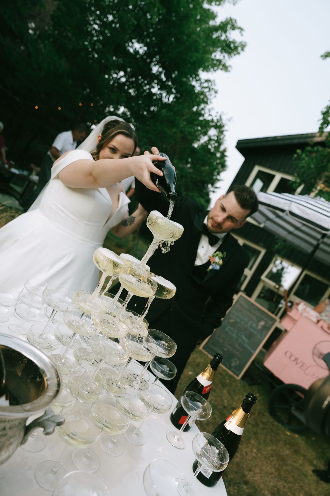 Elegant champagne tower being poured at an outdoor wedding celebration.