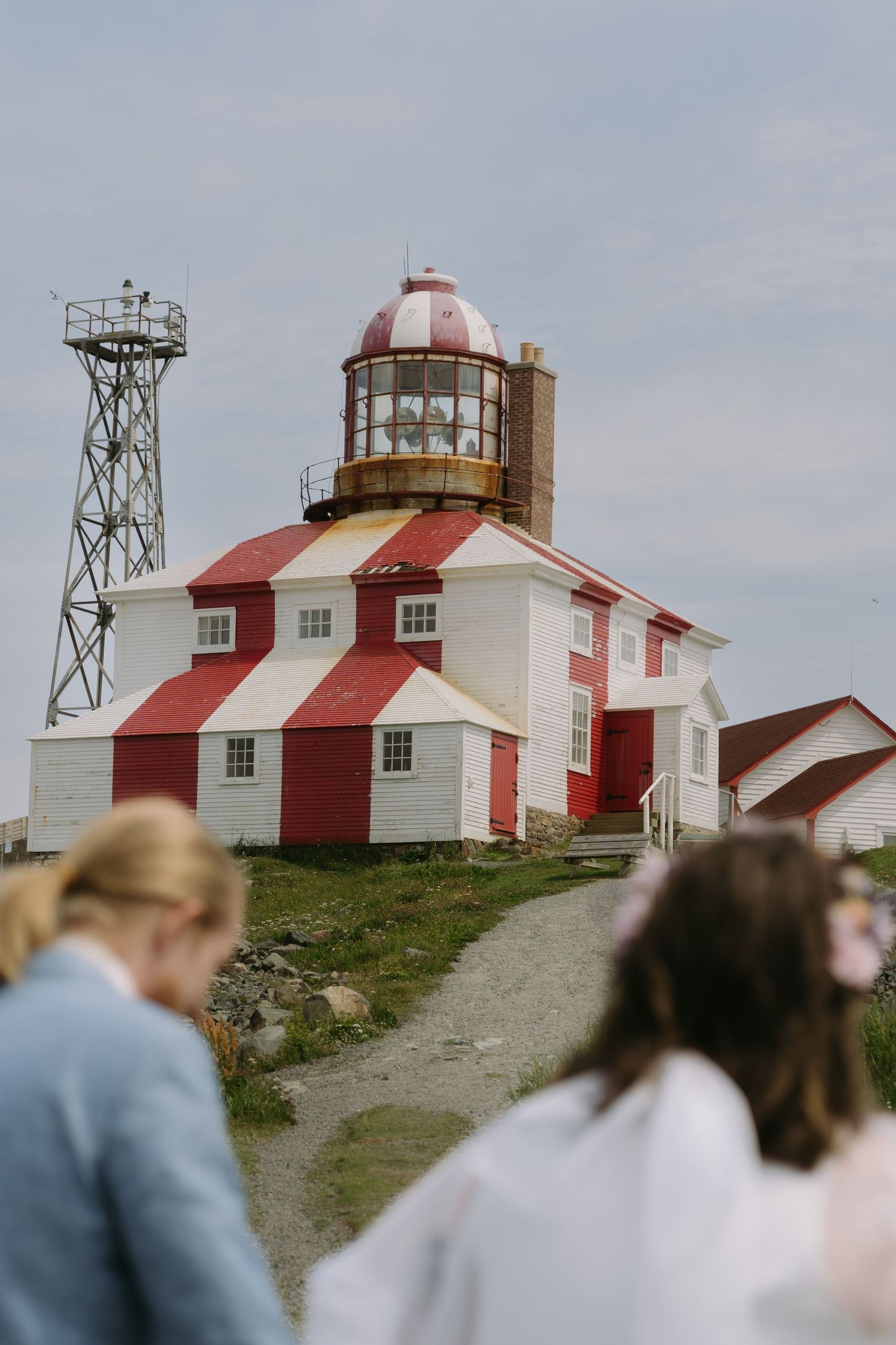 Red and white striped lighthouse buildings stand atop a grassy hill against a cloudy sky.