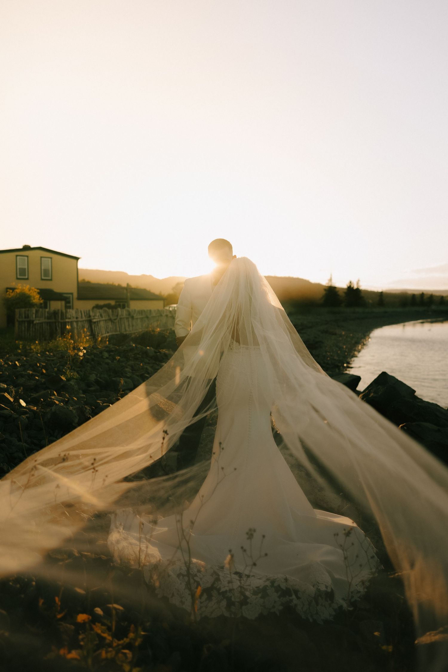 A flowing white veil catches golden sunlight against a coastal landscape at sunset creating an ethereal silhouette.