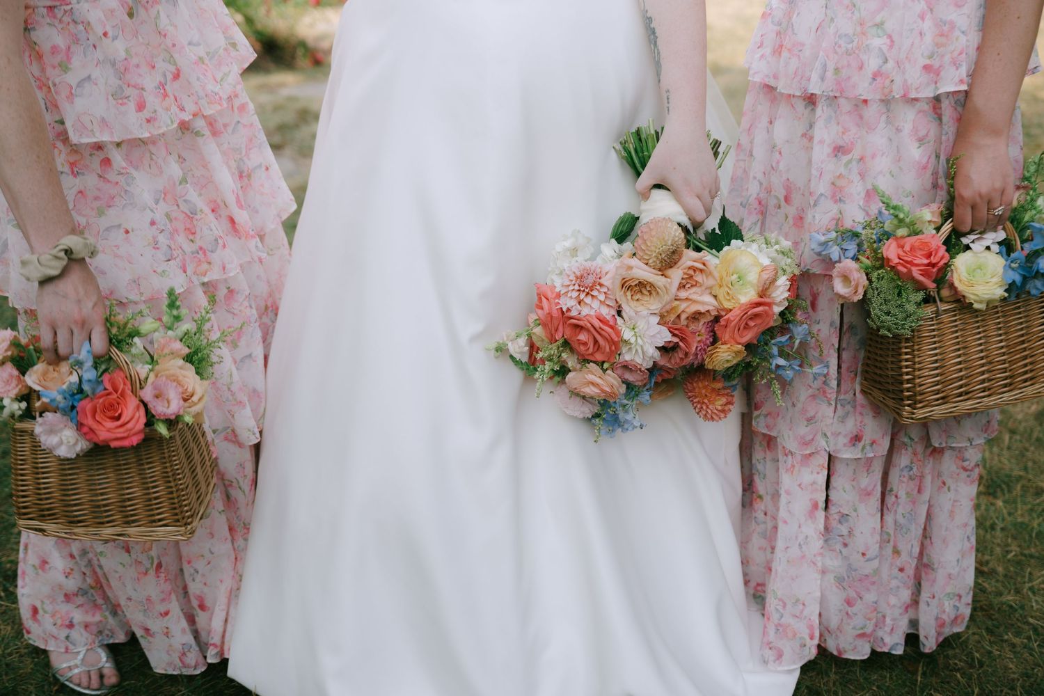 Bridesmaids in pink floral dresses holding bouquets outdoors.