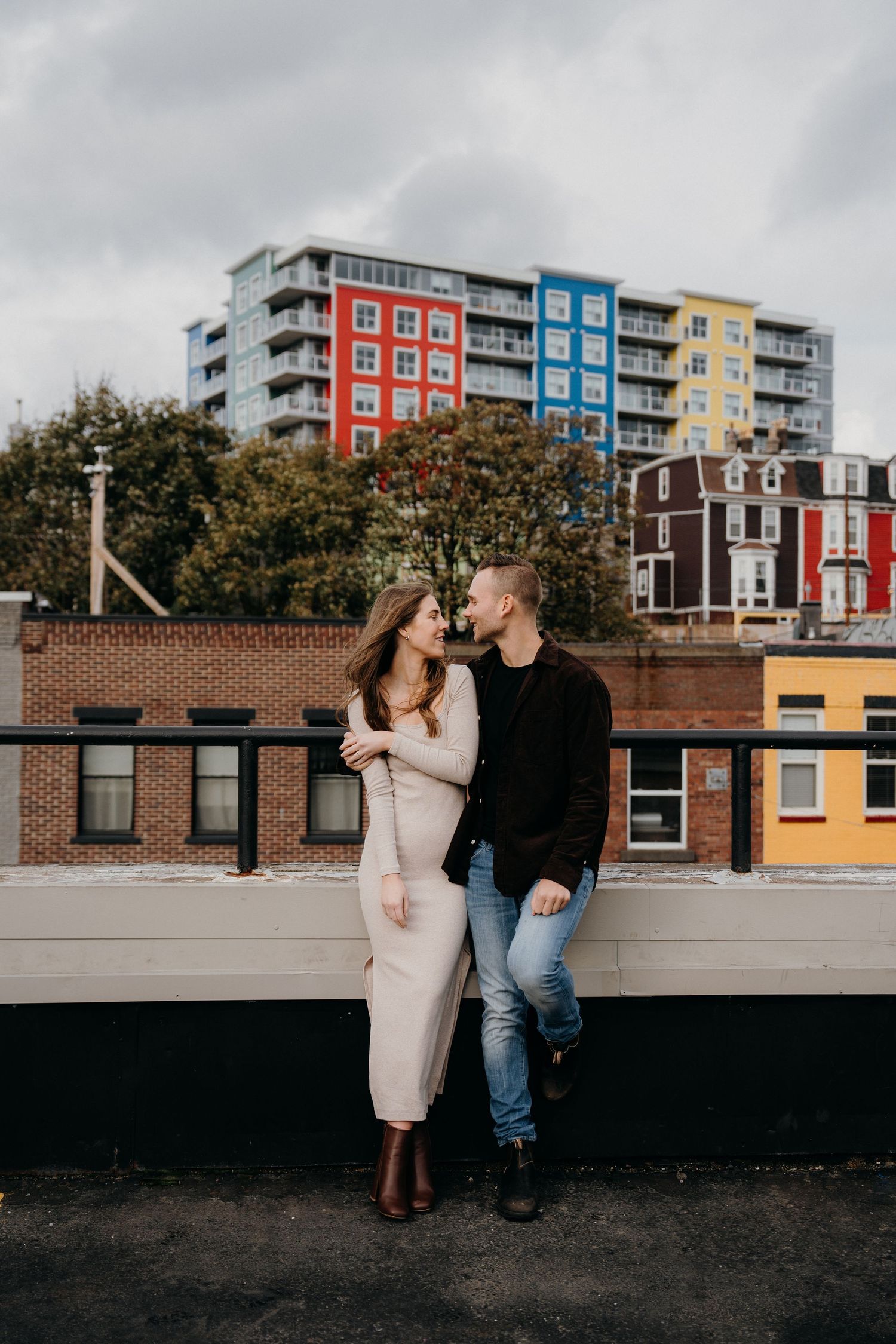 Couple posing against urban backdrop with vibrant multicolored buildings.