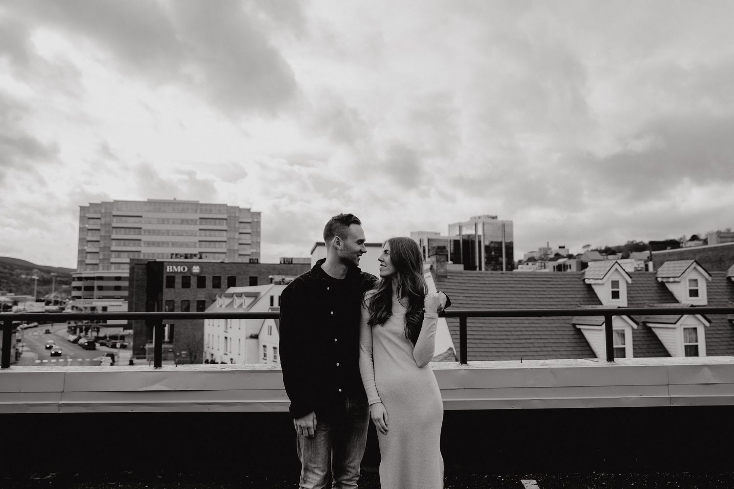 Black and white cityscape photo of couple standing together on rooftop parking area.