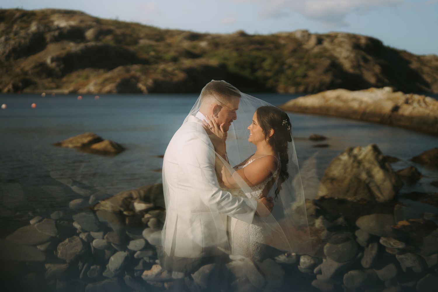 A couple shares a romantic moment on rocky coastal cliffs overlooking the ocean at sunset.