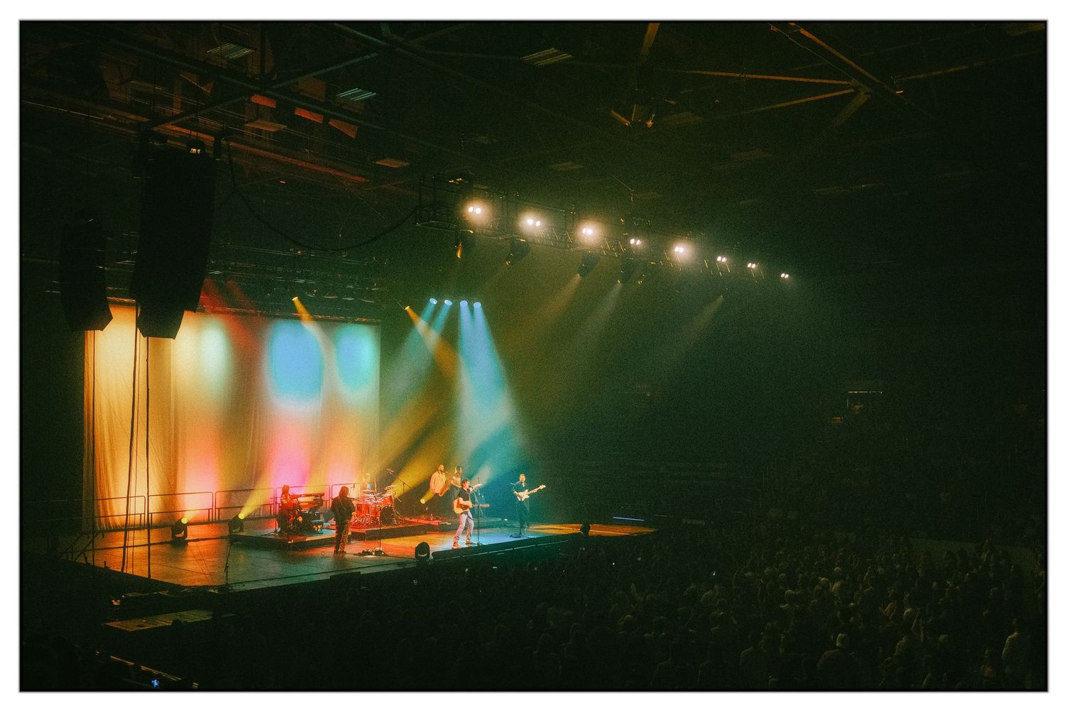 Musicians perform on a dimly lit concert stage with dramatic orange and blue lighting effects creating an atmospheric scene.