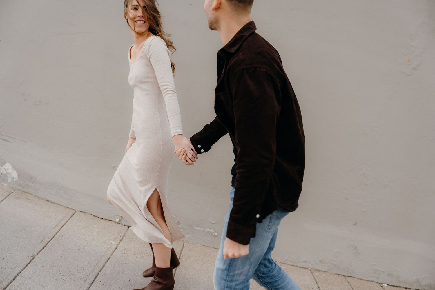 Couple in contrasting outfits posing elegantly against an industrial backdrop.