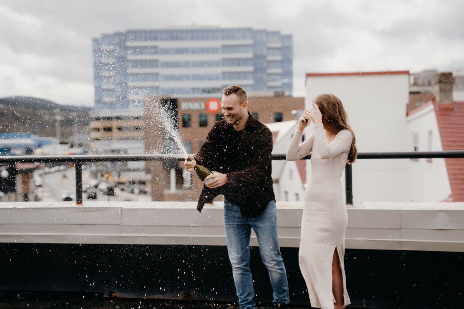 A couple shares a special moment on an urban rooftop with a dramatic cityscape behind them.