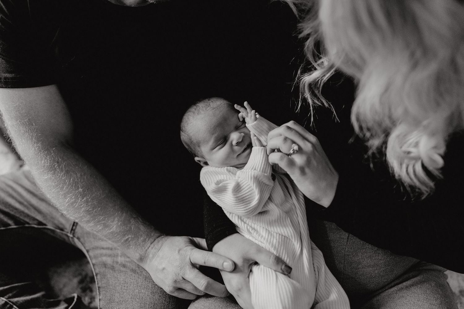 Intimate monochrome photograph of a newborn being cradled in soft light.