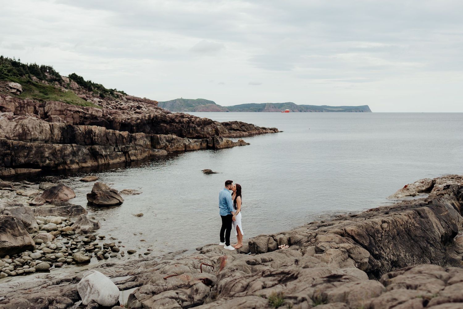 Wide panoramic view of a rocky coastline with distant cliffs and calm waters.