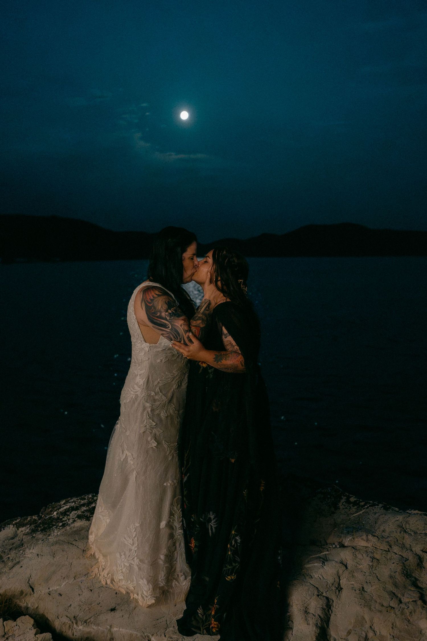 Couple shares intimate moment under full moon by waterfront.