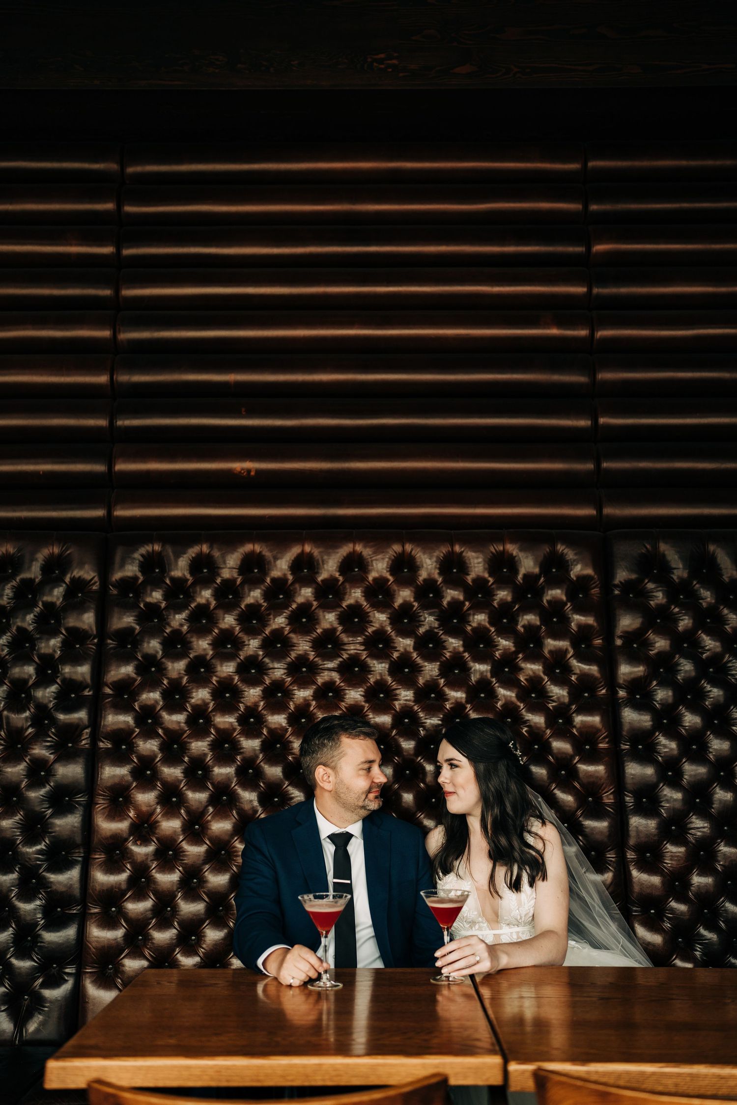 Couple sharing an intimate moment at a restaurant booth with brick wall and wine glasses.