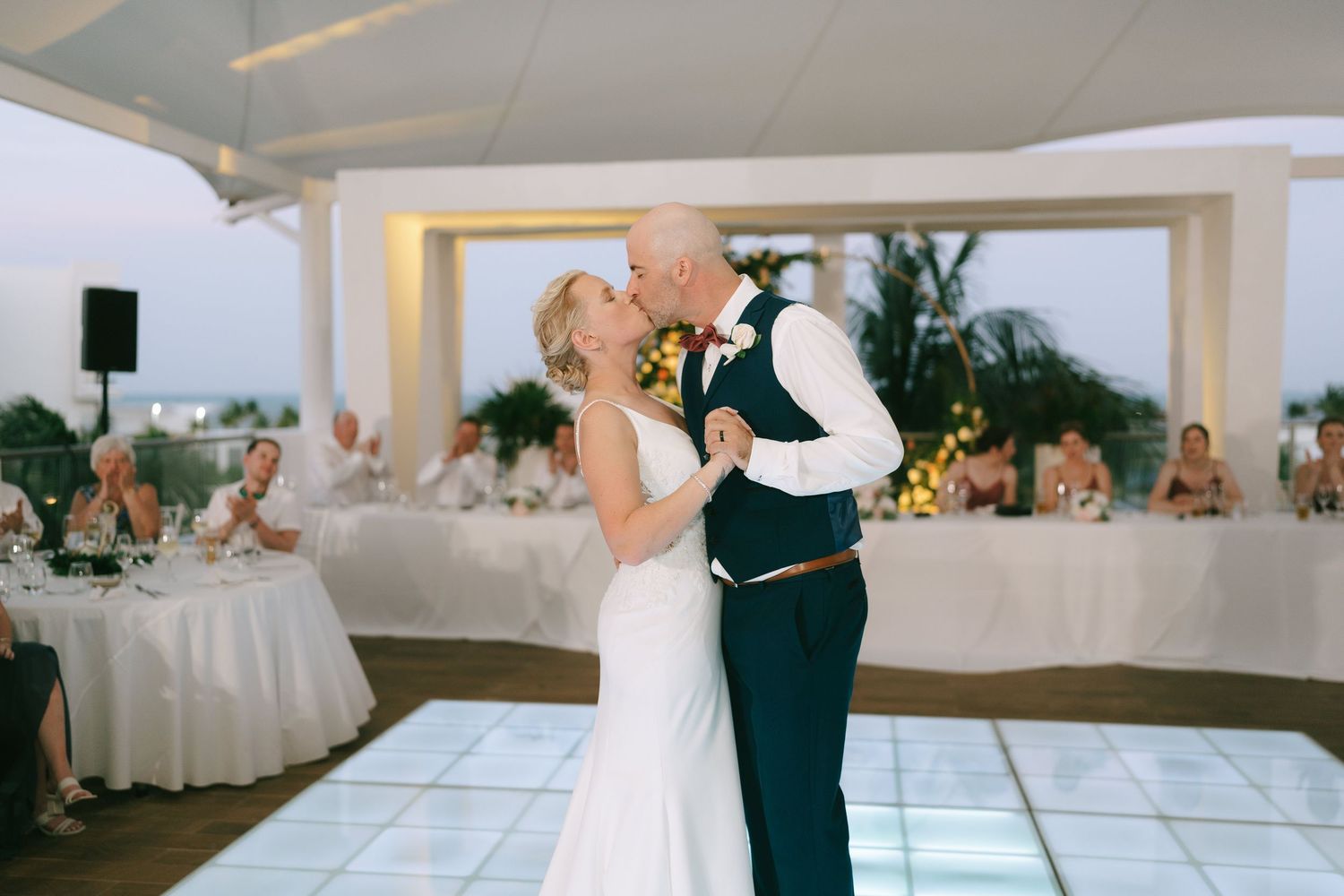 A couple shares a romantic dance in an elegant white ballroom setting during a wedding reception.