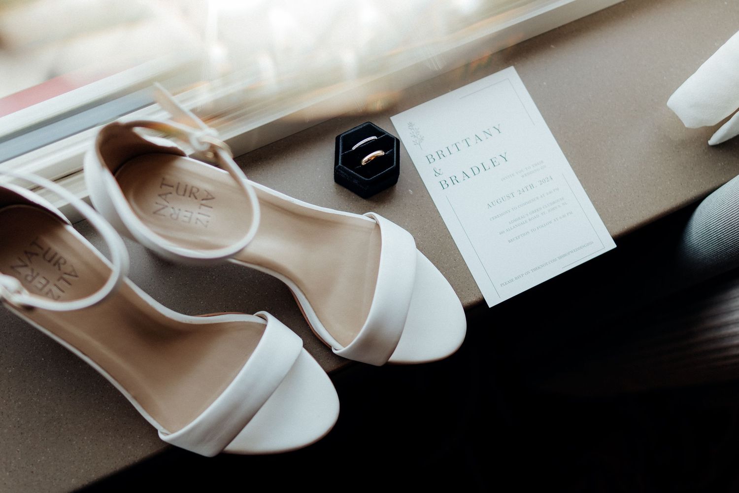 Elegant white bridal shoes and wedding stationery arranged on light surface.