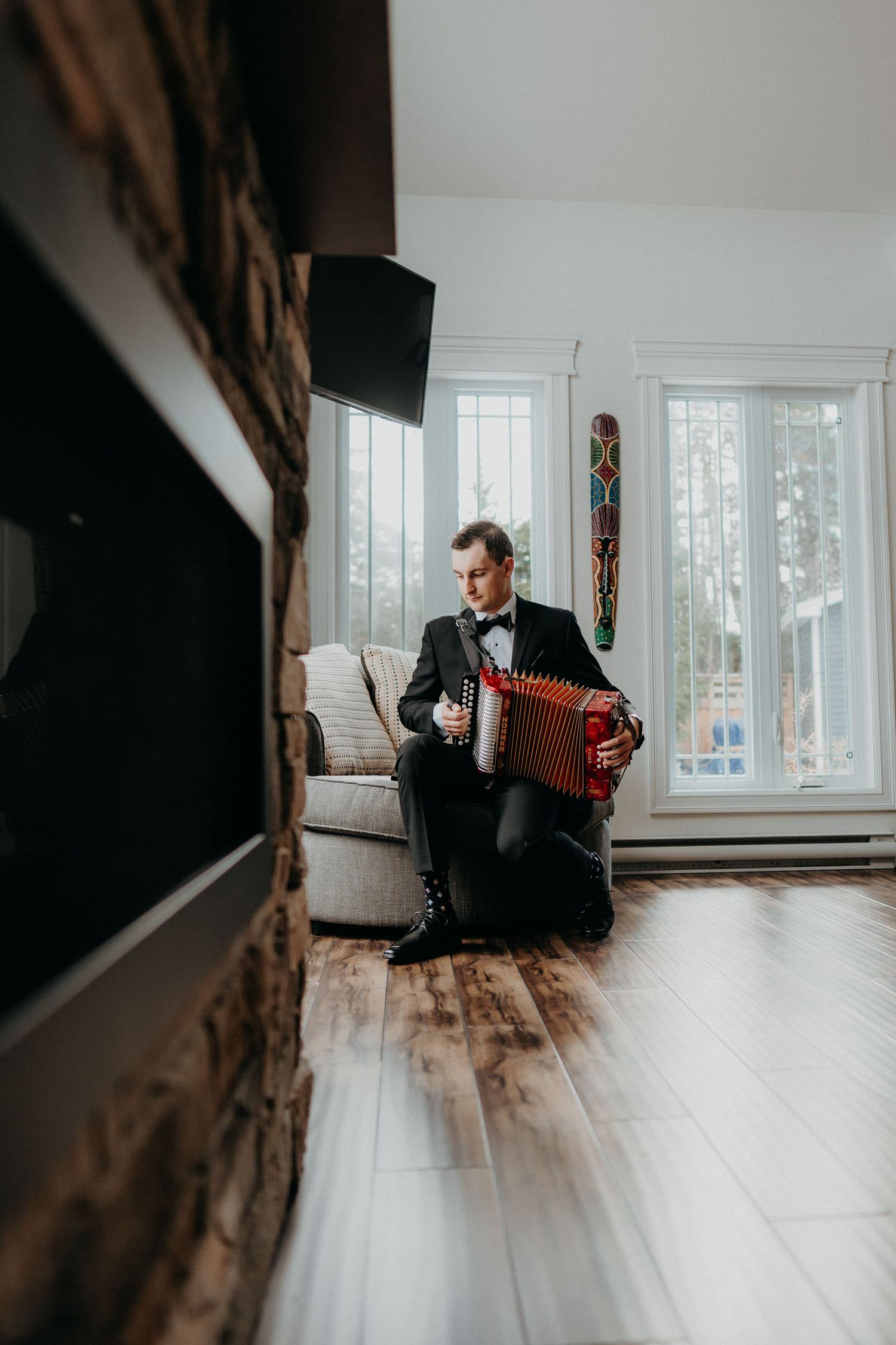 Person playing red accordion while sitting in minimalist room with wooden floors and bright windows.