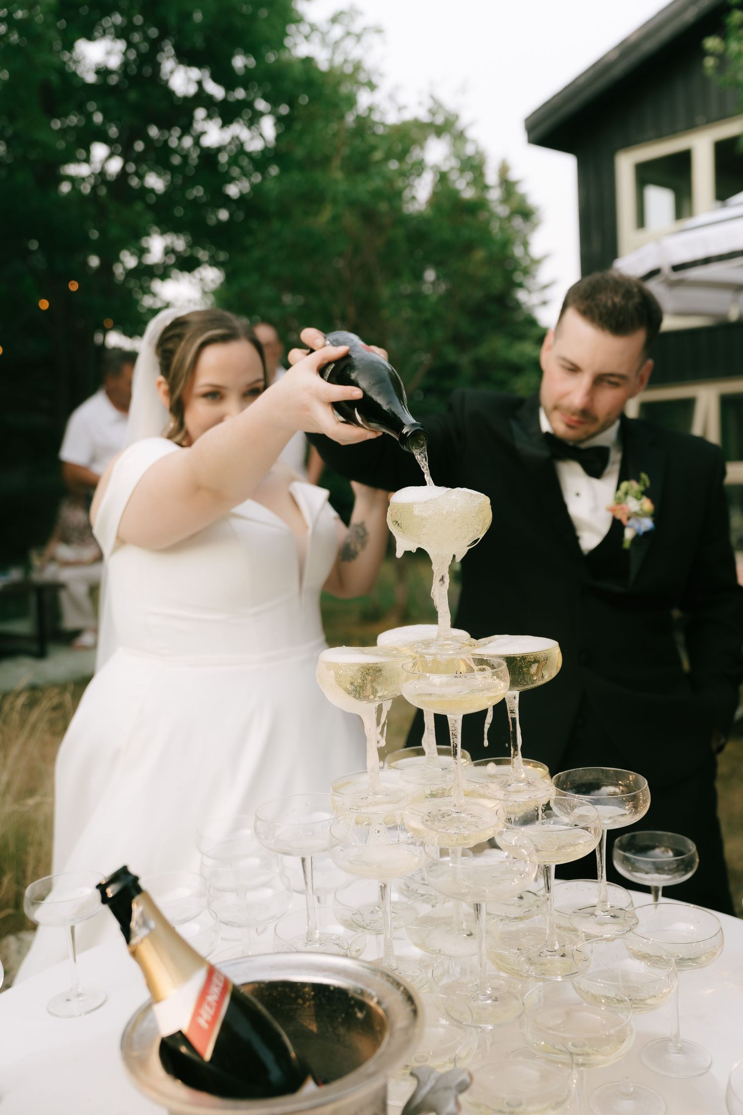 Champagne being carefully poured into a multi-tiered glass tower outdoors.