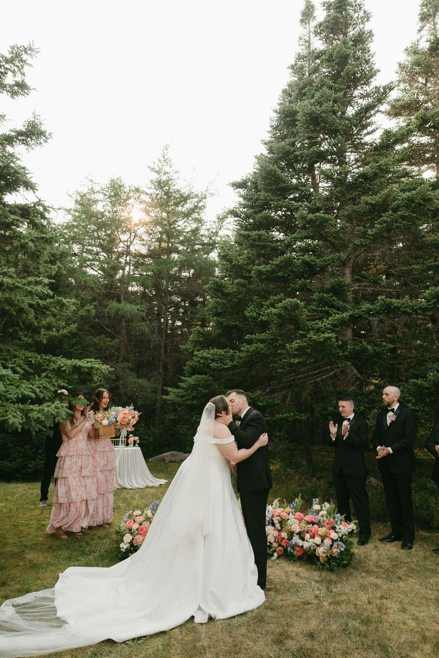Wedding party poses in front of pine trees during an outdoor forest ceremony.