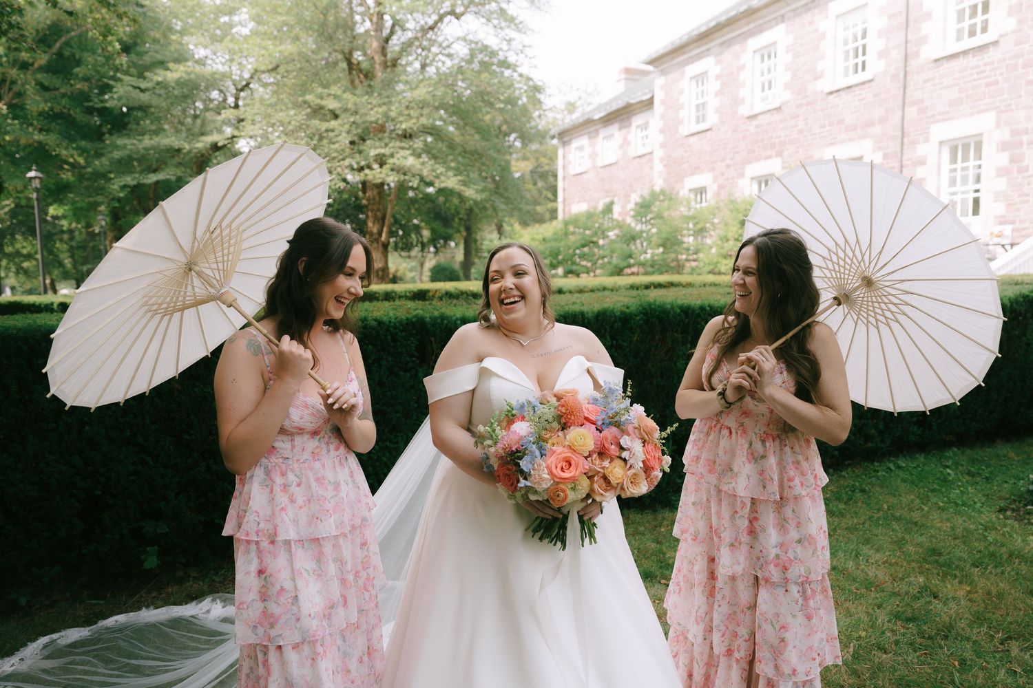 Wedding party with parasols poses outside historic brick building.