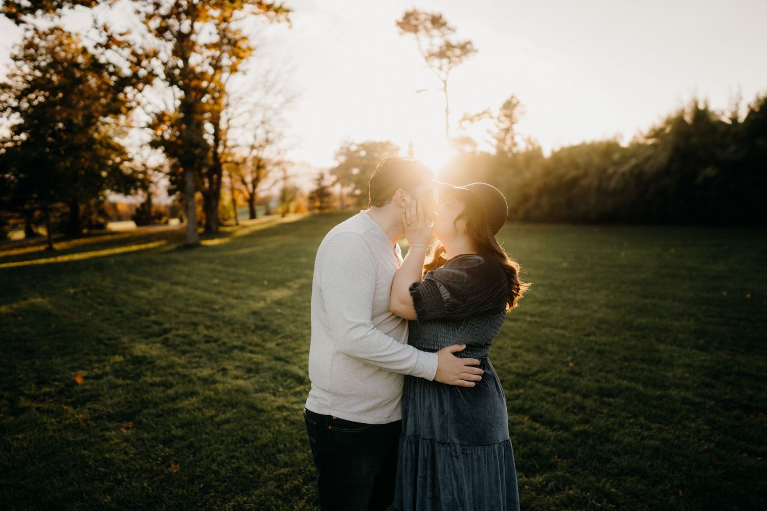 Intimate couple photoshoot in golden sunset light on grassy field.