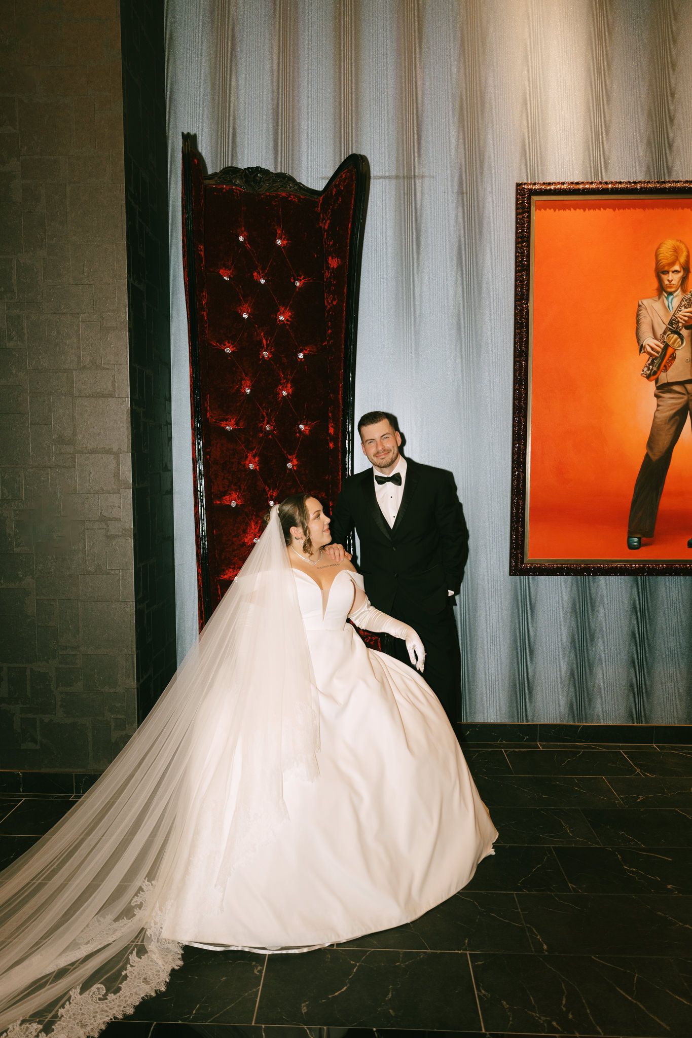 Wedding couple poses against modern interior with orange wall art and dramatic lighting.