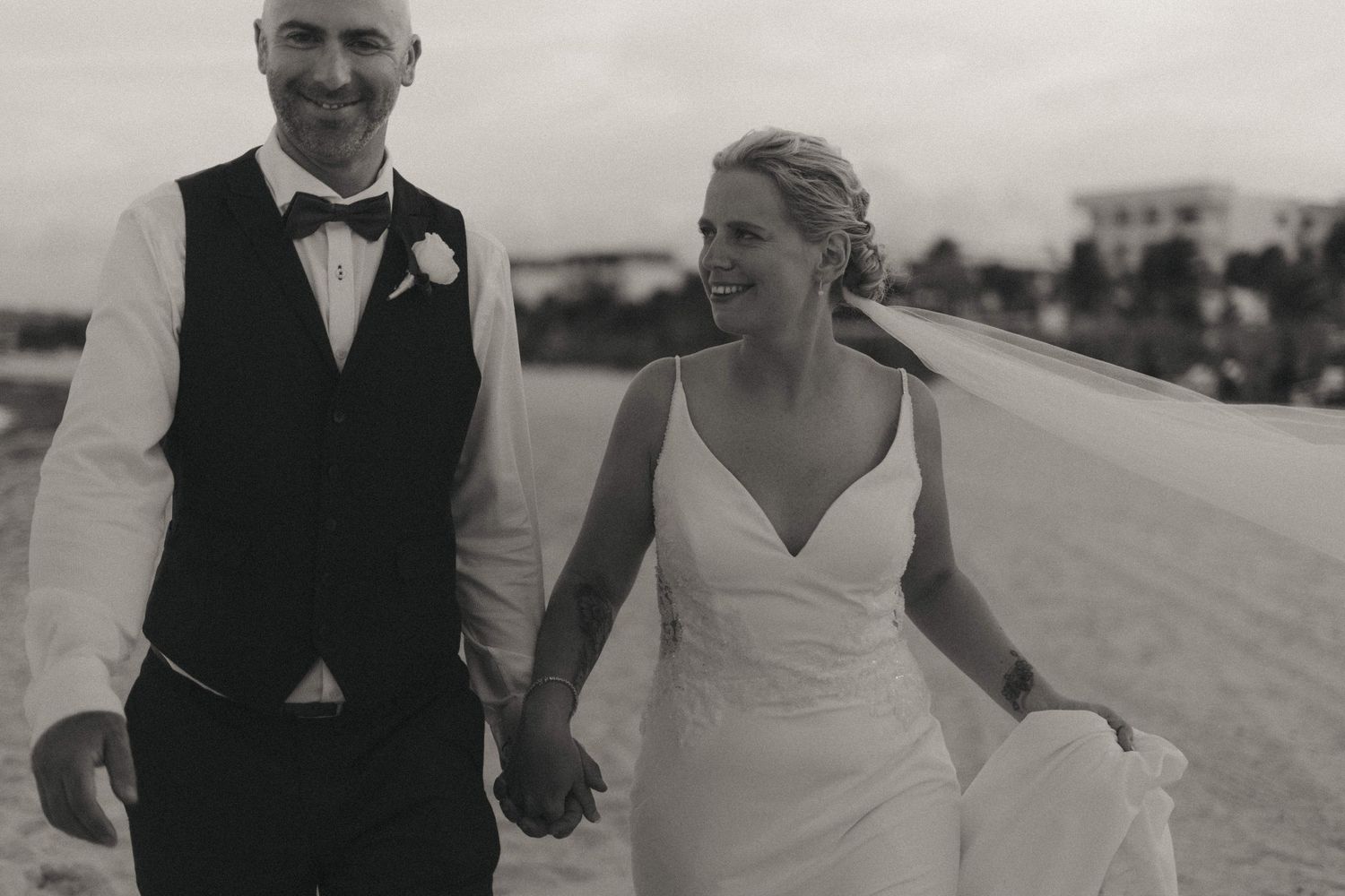 Newlyweds walking hand in hand along a sunny beach boardwalk.