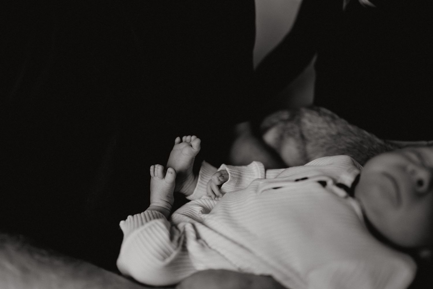Black and white image of a sleeping infant's tiny feet and hands.