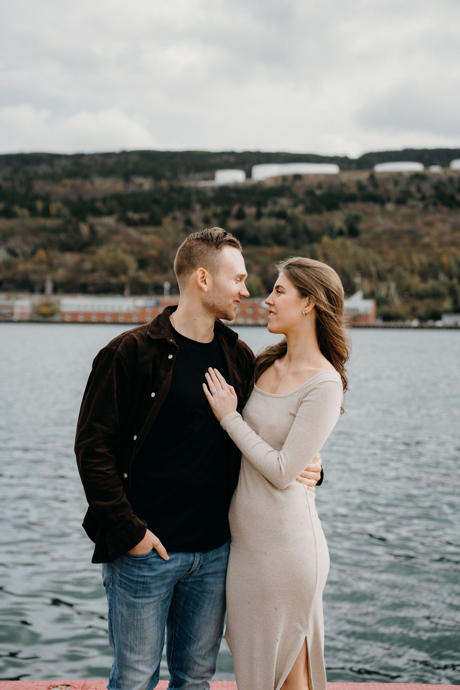 Romantic couple embracing on waterfront dock with autumn landscape in background.