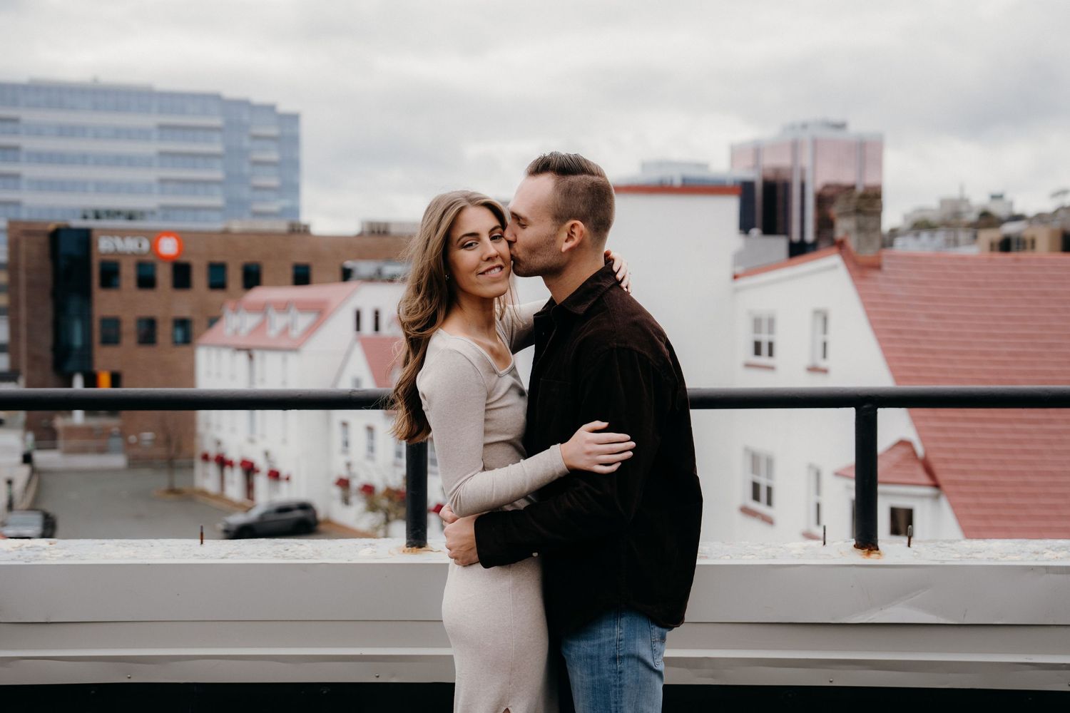 An intimate embrace shared between a couple during a rooftop photoshoot in an urban setting.