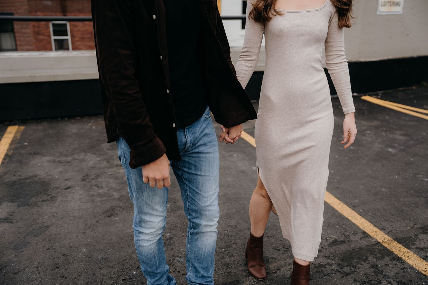 Two people stand together in a parking lot near brick buildings.