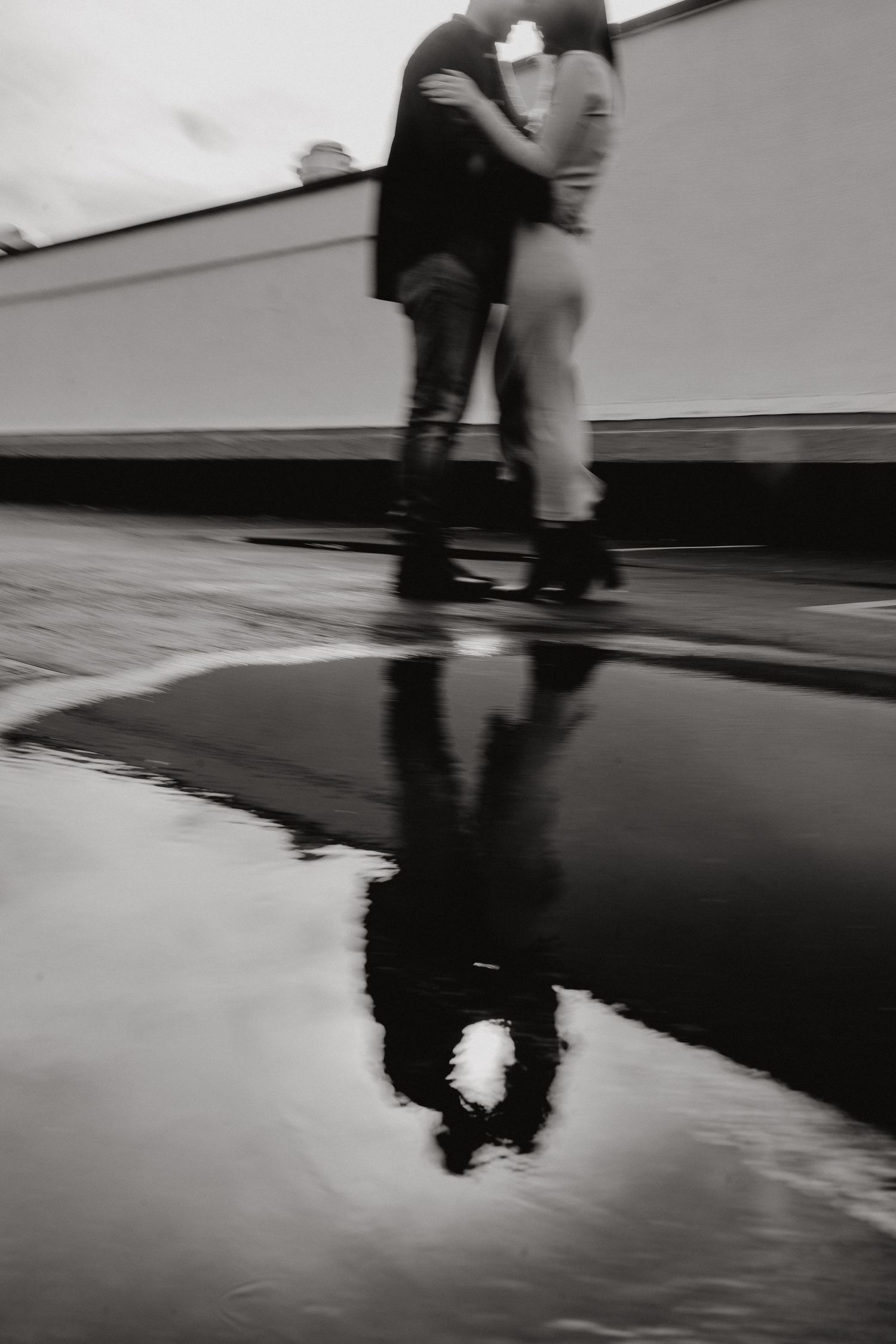 Motion blur photograph of figures walking across a reflective wet surface.