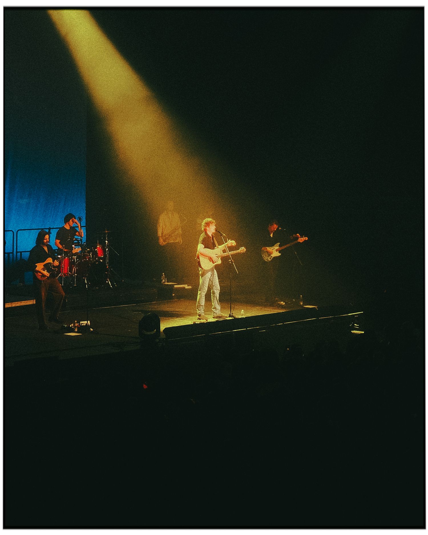 Musicians perform on a dimly lit stage with dramatic golden spotlights creating an atmospheric concert ambiance.