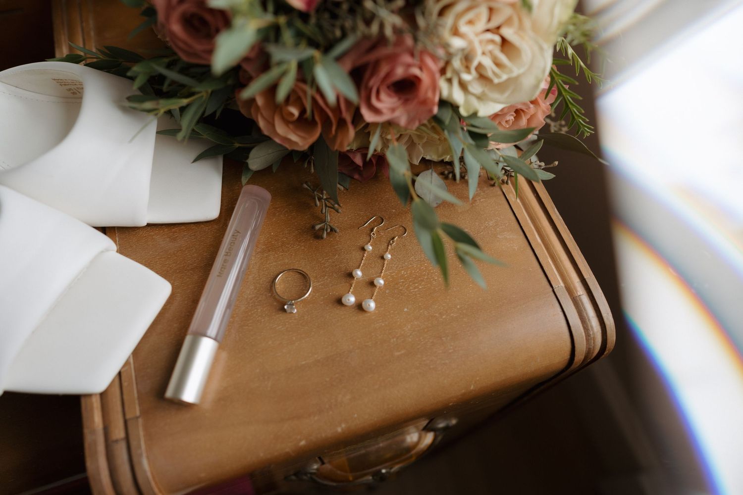 Pink and white roses with greenery lay atop a rustic wooden surface in soft natural lighting.