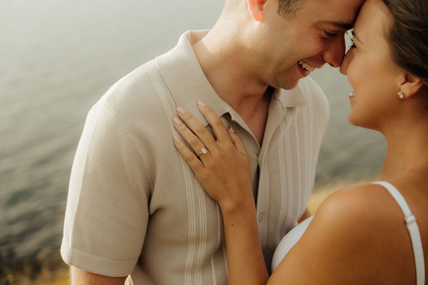 Romantic couple sharing intimate moments by the water during golden hour sunset.