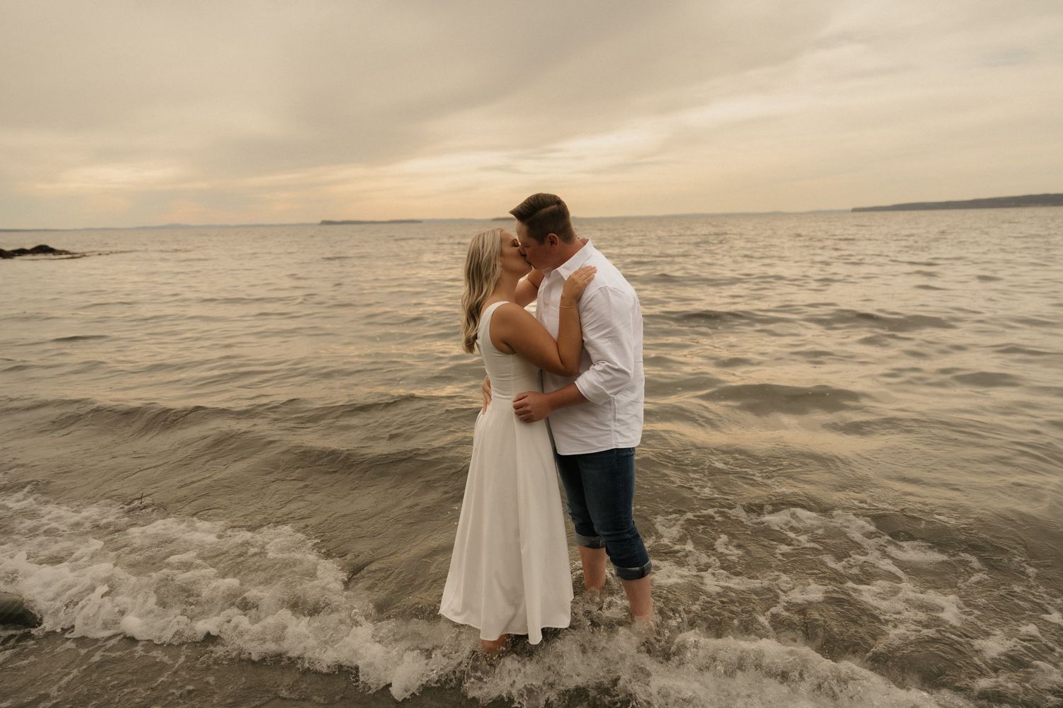 A couple shares a romantic moment at sunset on the beach as waves gently lap at their feet.