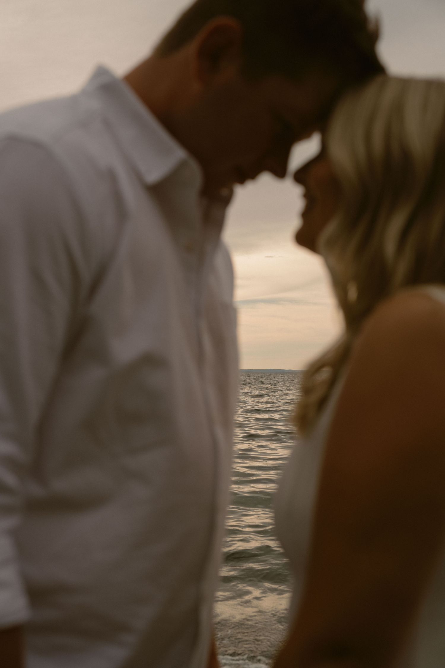 A romantic couple embraces against a serene ocean sunset backdrop, creating a silhouetted moment.