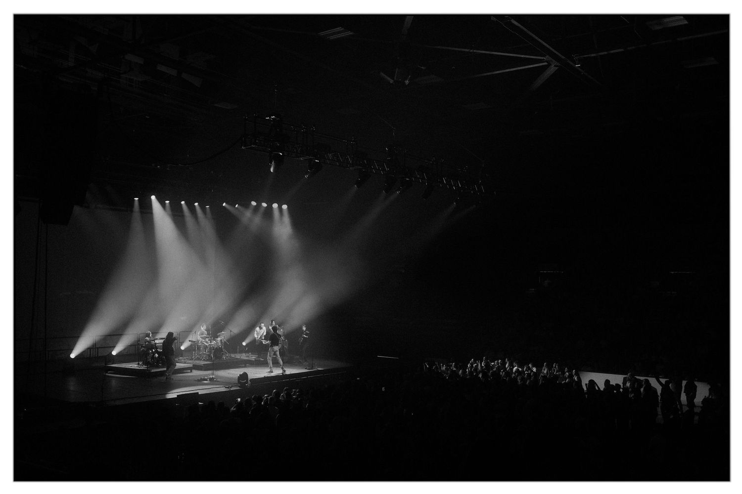 Silhouetted performers on a dimly lit stage with dramatic lighting and fog effects during a concert performance.