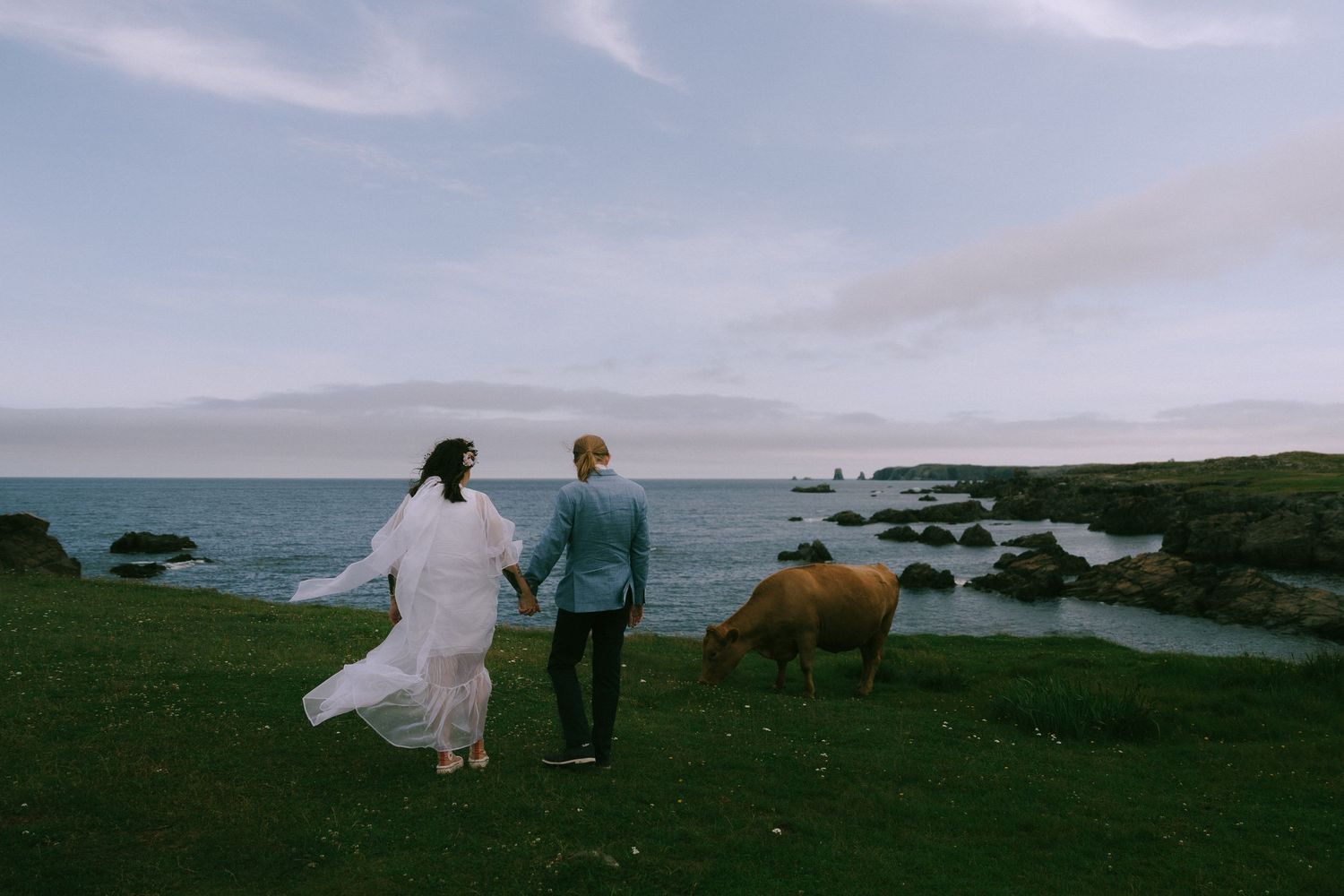 Couple walking along a scenic coastal path with dramatic cloudy skies and ocean views.