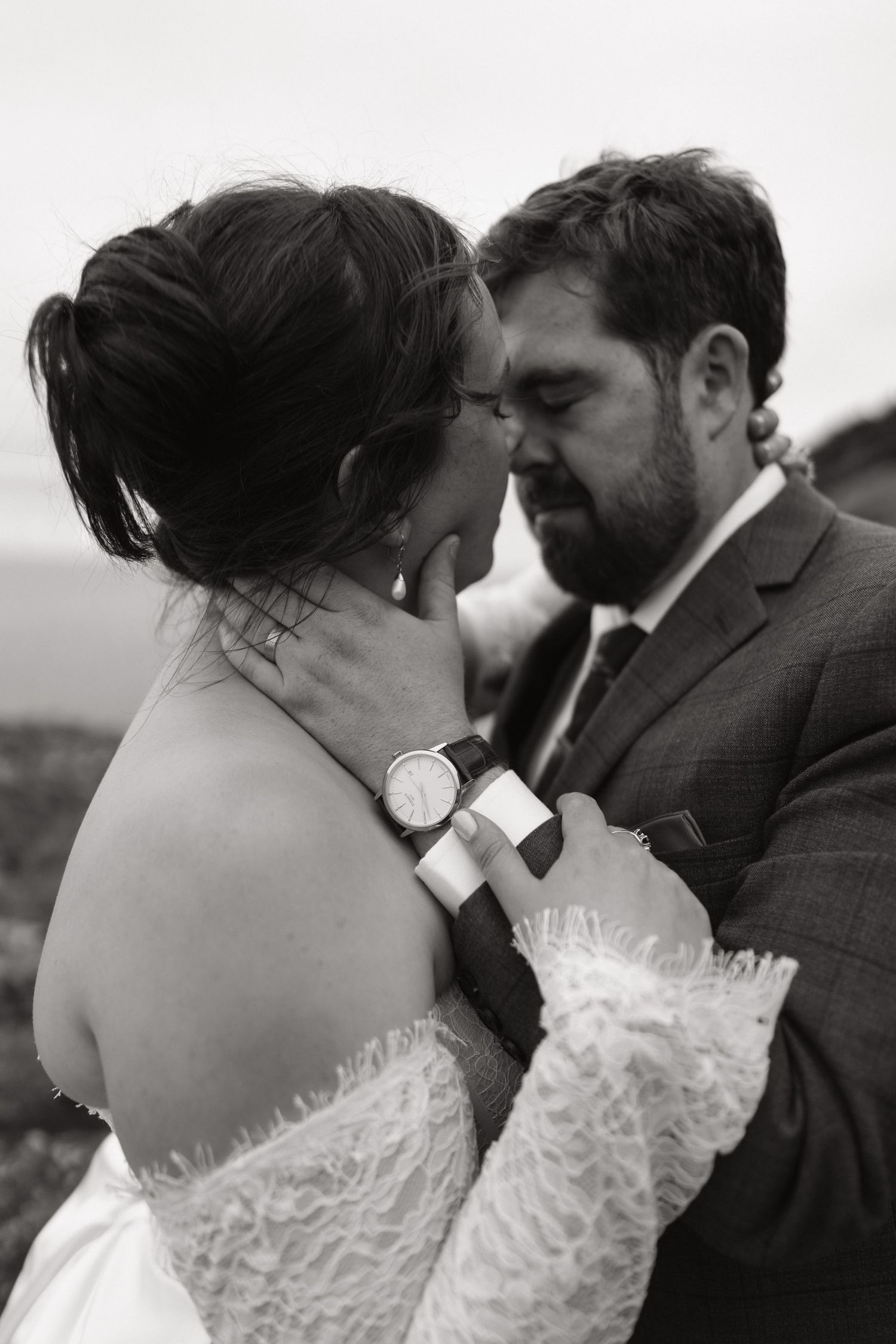 Black and white photo of a bride and groom sharing an intimate moment, groom tenderly holding bride's face.
