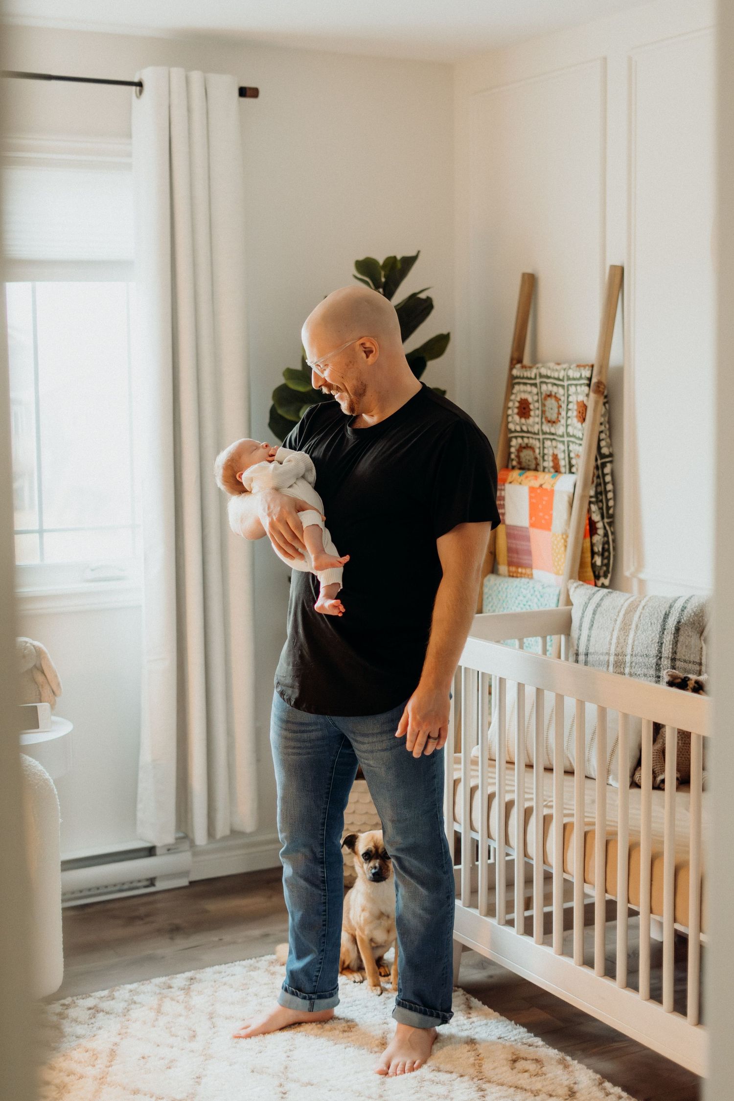 Individual holding baby while standing barefoot on patterned rug in nursery room.