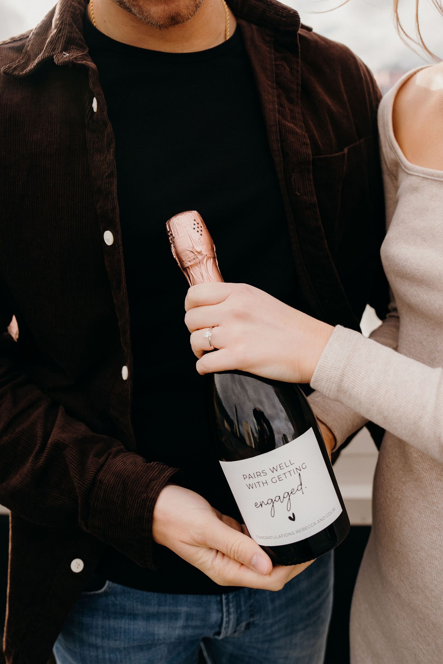 Close-up shot of hands holding an engagement celebration champagne bottle.